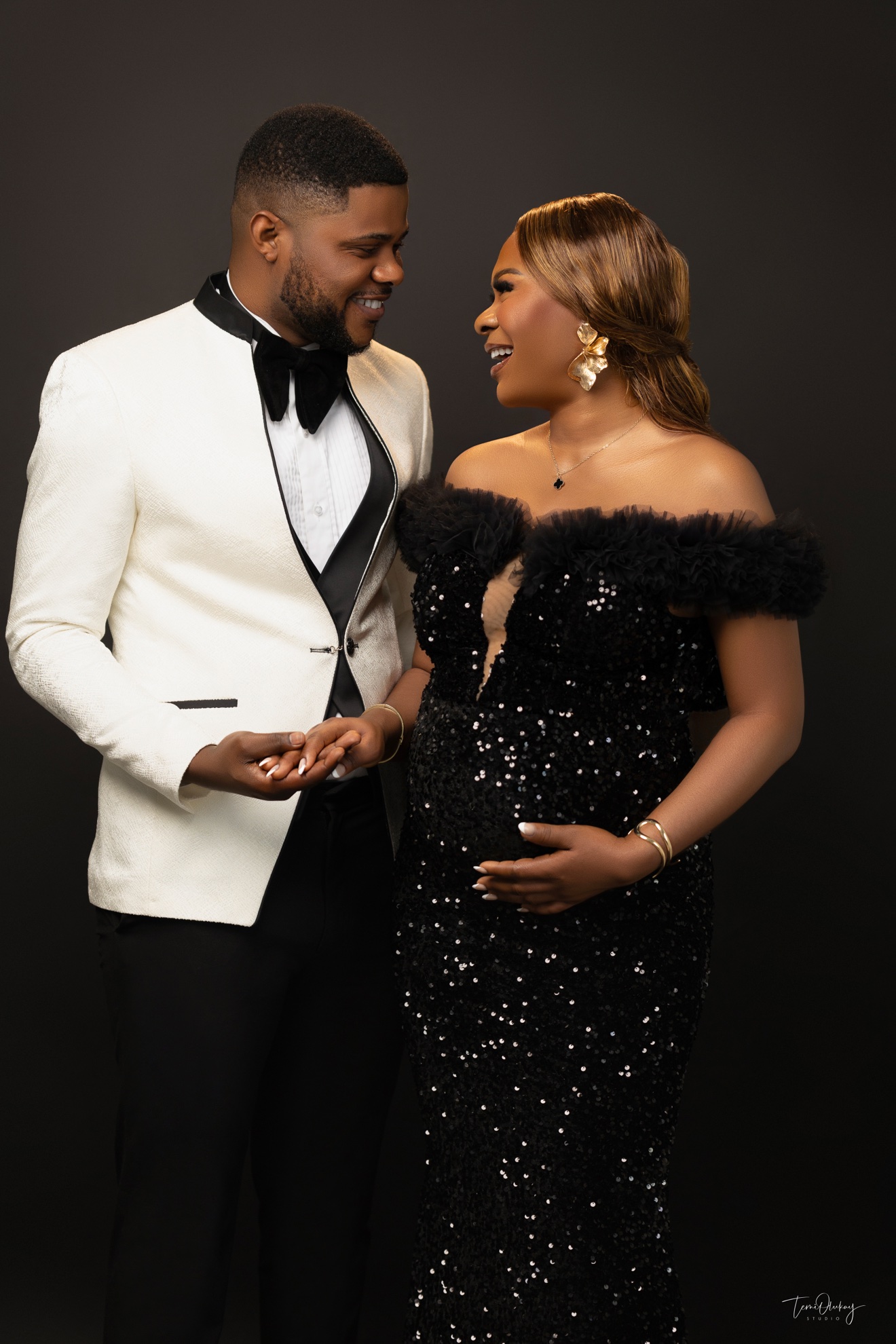 Couple maternity portrait, man in white tuxedo jacket and woman in black sequin gown