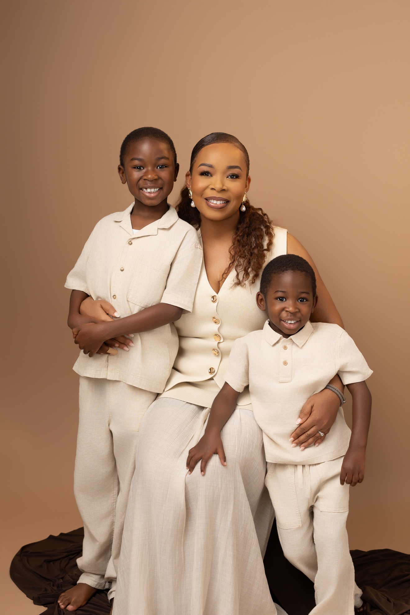 Family portrait, mother with her two young sons in cream linen on warm tan backdrop