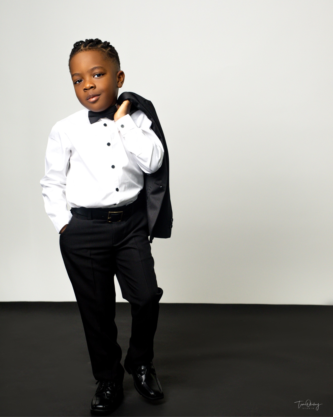 Young boy in white shirt, bow tie and black trousers, jacket slung over his shoulder