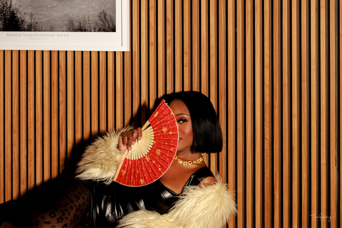 Editorial portrait holding a red fan, wearing cream fur against a wood-slat wall