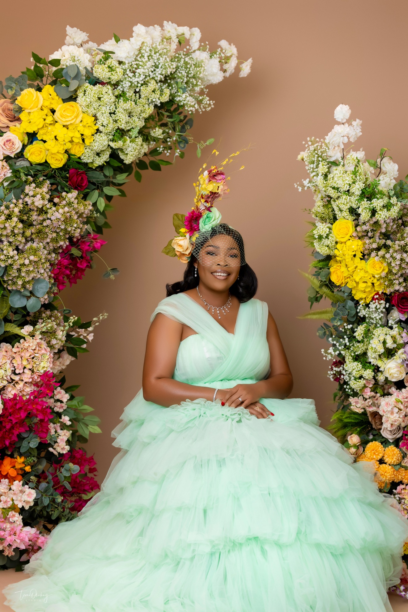 Portrait in mint green tulle gown seated between colourful floral arrangements