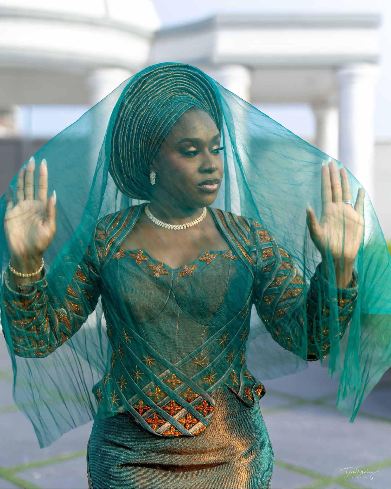 Woman in teal traditional attire holding a sheer veil over her face